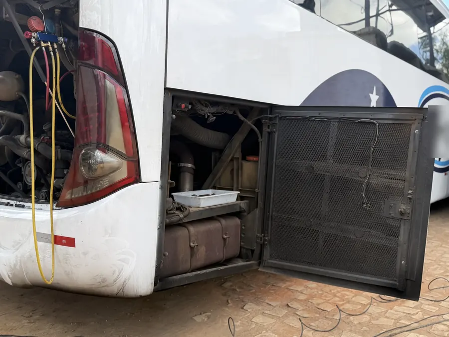Compartimento lateral do ônibus aberto para manutenção do ar-condicionado, com o manifold ligado na traseira