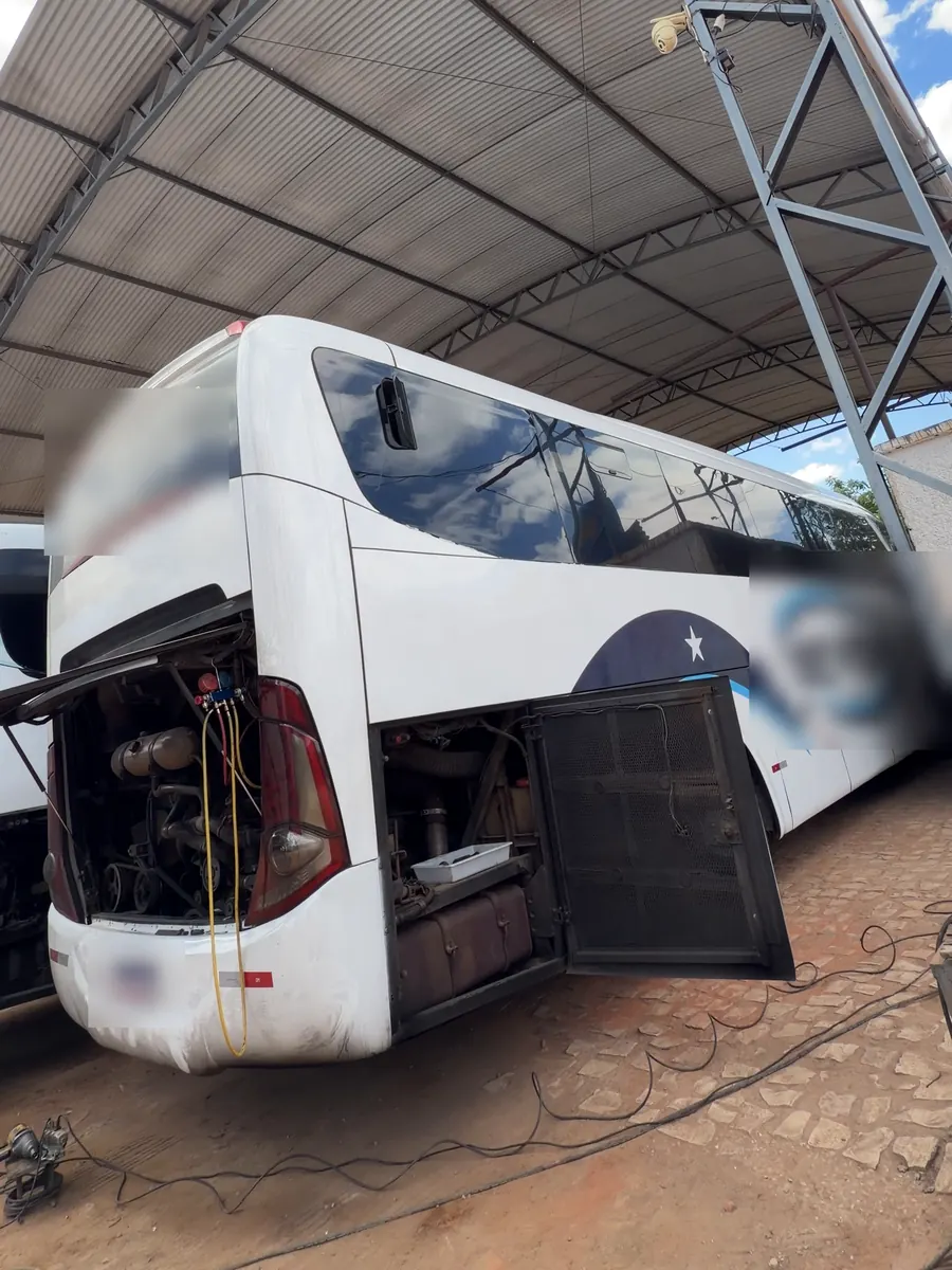 Ônibus rodoviário na oficina da JS Eletrofrio, com a tampa traseira e o compartimento lateral abertos, debaixo da cobertura metálica