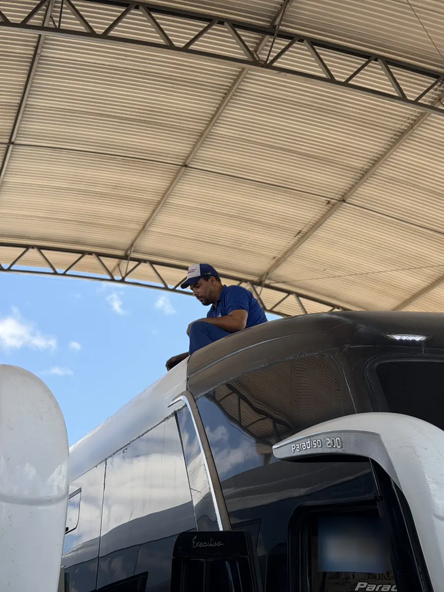 Técnico trabalhando no teto de um ônibus rodoviário na oficina da JS Eletrofrio, debaixo da cobertura metálica